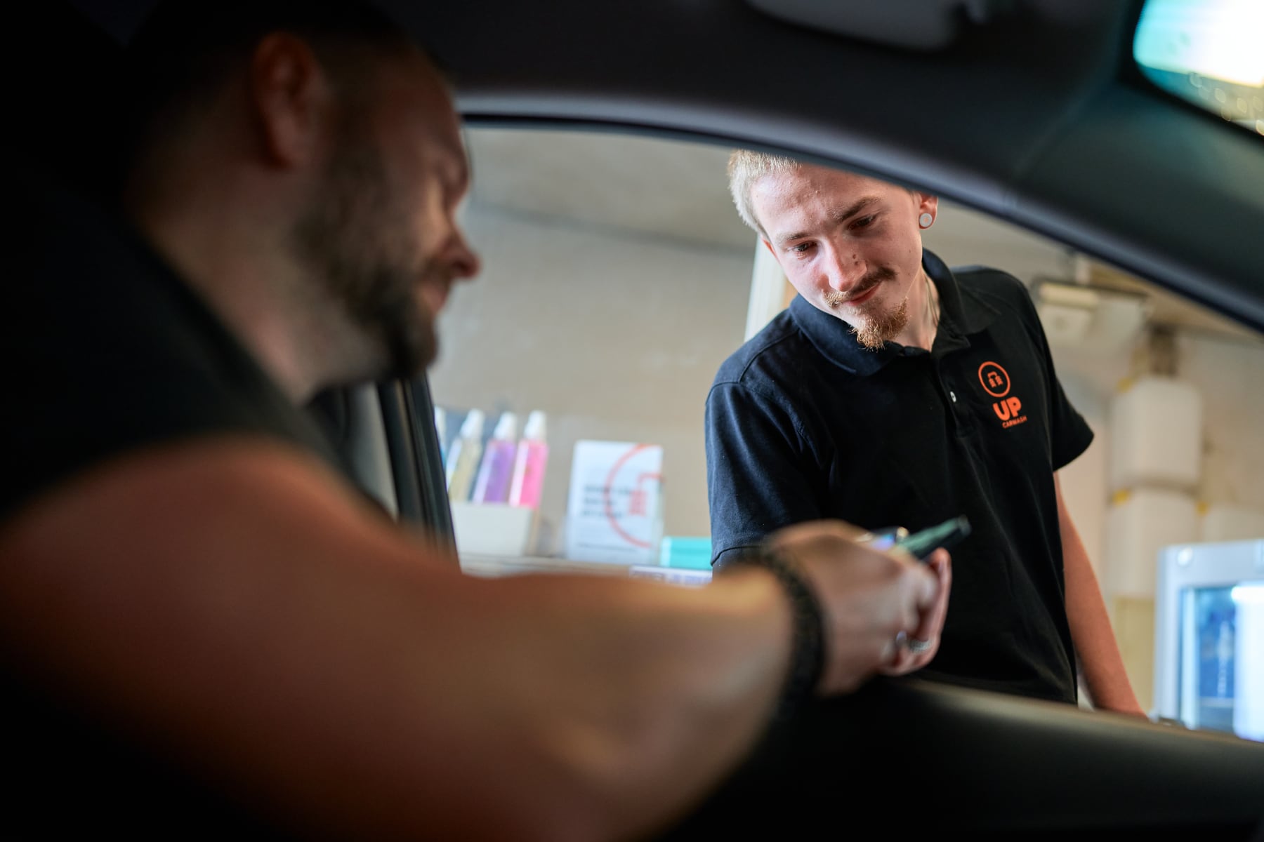 Een medewerker van UP geeft een klant door het autoraam de pas terug